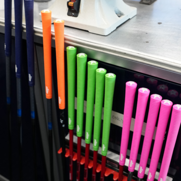 Colorful golf club grips displayed on a rack in a workshop setting.